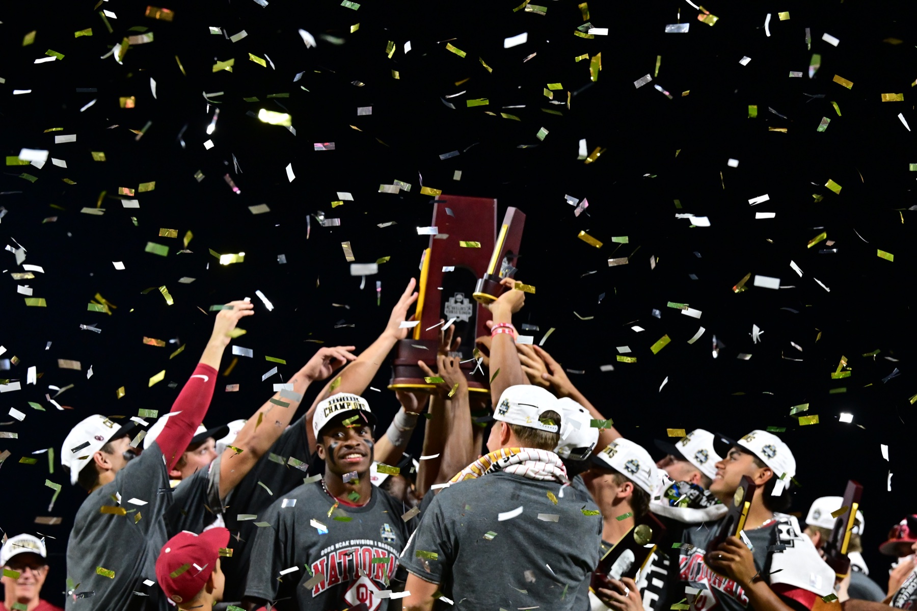 Oklahoma players lifting the NCAA Division I Baseball National Championship trophy under falling confetti
